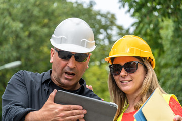 Work problem. Two scared, disappointed and surprised construction workers (male and female) reading bad news on the digital tablet