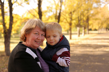 Fototapeta na wymiar Portrait of a happy grandmother with a charming little grandson in the autumn Sunny Park on the background of yellow trees.