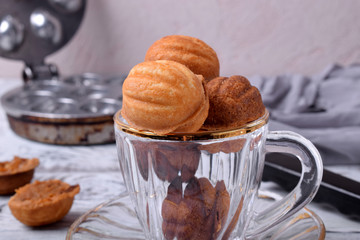 Walnut shaped cookies with caramel in a glass cup on the white table. Special skillet in the background