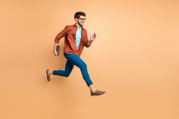 Fototapeta na wymiar Full length body size view of his he nice attractive cheerful glad guy leader jumping in air carrying laptop running fast late hurry-up meeting appointment isolated over beige color pastel background