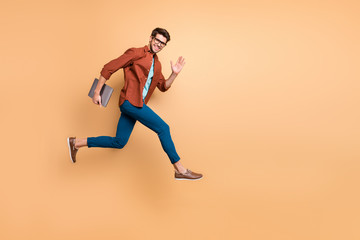 Fototapeta na wymiar Full length body size view of his he nice attractive cheerful cheery glad content guy jumping in air carrying laptop running fast late hurry-up meeting isolated over beige color pastel background