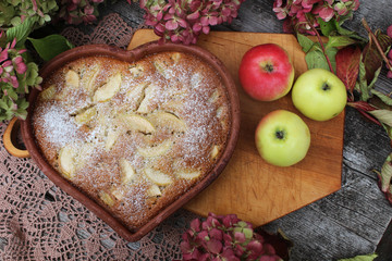Apple pie in the form of a heart on a wooden background, hydrangea flowers, top view. The concept of home food, healthy food, comfort, warmth. Rustic style of life, autumn.
