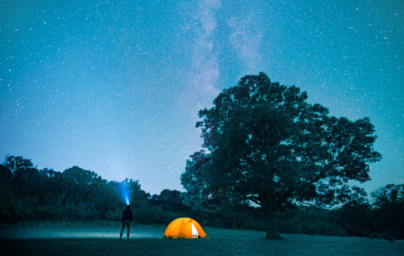 man camping with tent in forest at night with starry sky