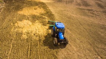 Obraz premium aerial view drone of blue tractor with plow in operation in the field