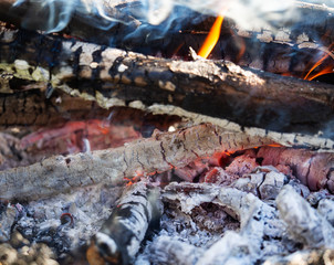 Glowing embers in the ash with log in smoke, closeup