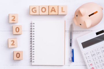 2020 goal, finance plan abstract design concept, wood blocks on white table background with piggy bank and calculator, top view, flat lay, copy space.