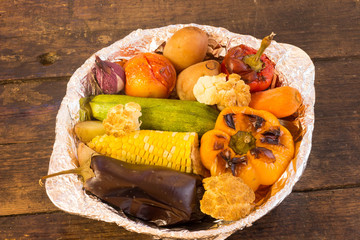 Baked vegetables in foil potato carrot pepper onion corn on the cob eggplant cauliflower squash on wooden table