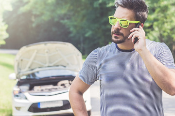 Fototapeta premium Man talking on mobile phone and broken car in the background
