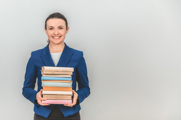 Lovely female teacher holding a stack of colorful books, smiling.