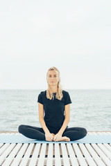 Young pleasant caucasian woman in sportswear is sitting in lotus position after exercise outdoors.