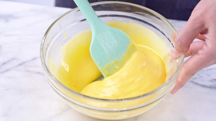 Mixing egg yolk into cake batter with green rubber spatula mixer tool stirring until smooth and blend well in a glass bowl, close up, lifestyle - obrazy, fototapety, plakaty