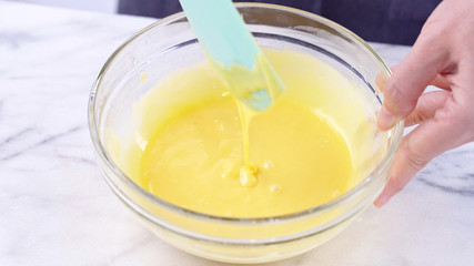 Obraz na płótnie Canvas Mixing egg yolk into cake batter with green rubber spatula mixer tool stirring until smooth and blend well in a glass bowl, close up, lifestyle