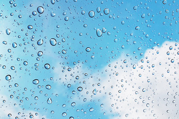 Water drops on glass with blue sky and clouds background. Abstract texture.