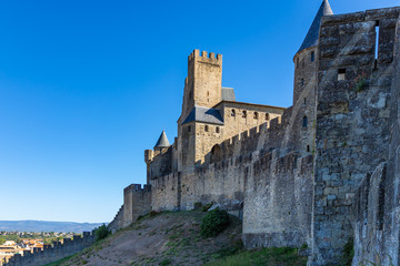 Outer wall of the fortified city of Carcassonne. Beautiful medieval castle at morning in the background of blue sky. High walls with towers of famous Cit&eacute; de Carcassonne. Occitanie region, France.