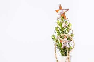 Little fir tree in ceramic vase with wooden decorations, toys. ribbon, ball, gift on white background. Christmas card.