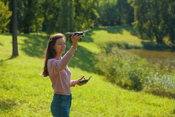 Young woman in a clearing in a park launches a drone, holding an aircraft in one hand and a control panel in the other. © Alexander