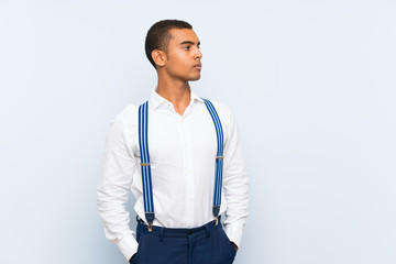 Young handsome brunette man with suspenders over isolated background looking side