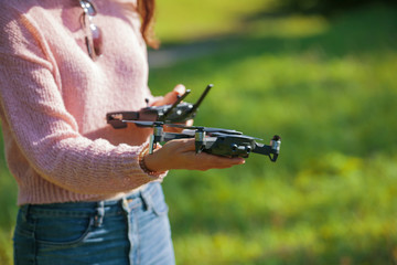 A young woman in a clearing in a park launches, checks, holds a drone, in one hand, in the other control panel. © Alexander