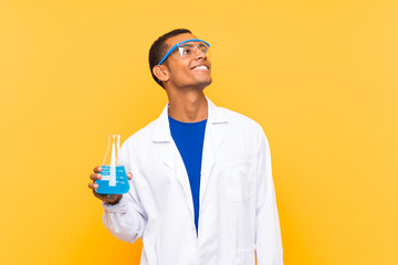 Scientific man holding a laboratory flask over isolated background looking up while smiling