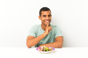 Young handsome man with salad in a table doing silence gesture