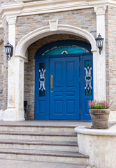 Modern entrance to the building, a ceramic pot with green heather. Large blue door. The entrance from the sidewalk to the building.