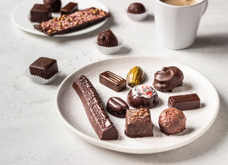 Coffee cup and assortment of fine chocolate candies on light grey stone background. 