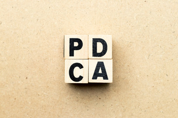 Alphabet letter block in word PDCA (business abbreviation of plan do check act) on wood background