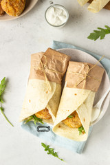 Tortilla wraps with chicken or turkey cutlets, arugula and sour cream sauce on a ceramic plate.