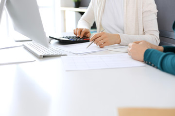 Obraz na płótnie Canvas Accountant checking financial statement or counting by calculator income for tax form, hands close-up. Business woman sitting and working with colleague at the desk in office. Audit concept
