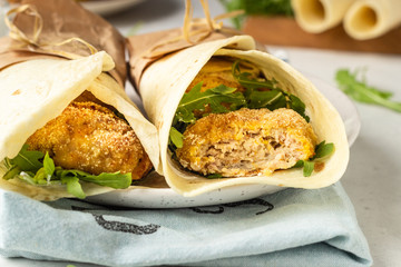 Tortilla wraps with chicken or turkey cutlets, arugula and sour cream sauce on a ceramic plate.