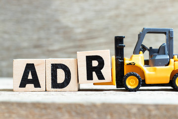 Toy forklift hold letter block r to complete word ADR (Abbreviation of Adverse drug reaction) on wood background