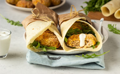 Tortilla wraps with chicken or turkey cutlets, arugula and sour cream sauce on a ceramic plate.