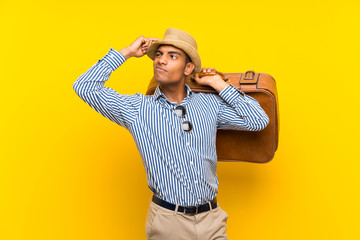 Brunette man holding a vintage briefcase over isolated yellow background having doubts and with...