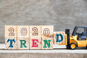 Toy forklift hold letter block d to complete word 2020 trend on wood background