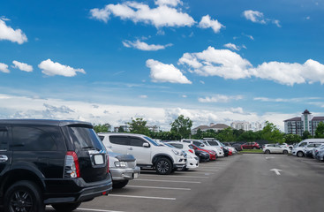 Fototapeta na wymiar Car parking in large asphalt parking lot with trees, white cloud and blue sky background