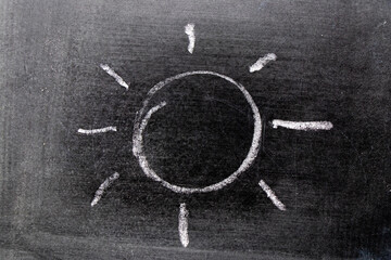 White color chalk hand drawing in sun with ray shape on blackboard background