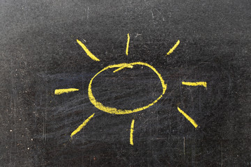 Yellow color chalk hand drawing in sun with ray shape on blackboard background