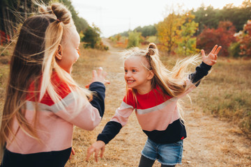 Twin blondes walk and have fun in the autumn forest among the red trees.