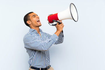 Young handsome brunette man over isolated blue background shouting through a megaphone