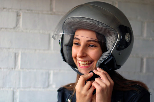 Girl dressed in a leather jacket, putting on a grey motorcycle helmet.