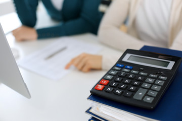 Calculator and binders with papers are waiting to be processed by business woman or bookkeeper working at the desk in office back in blur. Internal Audit and tax concept