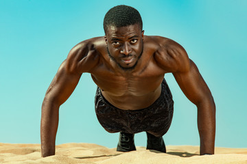 Young sportsmen man, fit athlete doing pushups in the desert on a background of blue sky. Healthy lifestyle, sport fashion. Guy in black sportswear. Fitness concept.