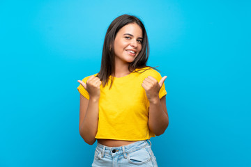 Young girl over isolated blue background with thumbs up gesture and smiling