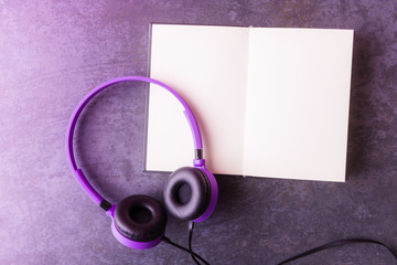 Flat lay of violet  headphones and open blank notebook