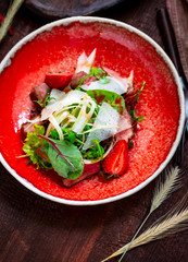 Warm salad of beef tenderloin, arugula, spinach, strawberries and Parmesan in a red plate on a wooden background. Italian cuisine rustic style