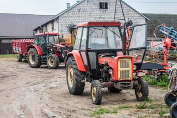 Obraz premium Red tractors and agricultural equipment in the yard of a dairy farm. Cowshed in the background. Podlasie, Poland.