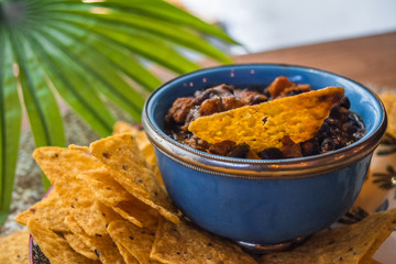 Plato de nachos con un bol de salsa de frijoles con nachos  y una hoja de palma de fondosumergidos dentro