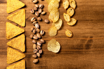 Variety of beer snacks lie in a row on a wooden table, top view, flat lay. Nachos, pistachios, chips and other beer snacks on a wooden background