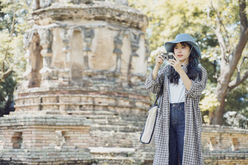 Fototapeta na wymiar Young asian female traveler taking a photo with retro camera while traveling in popular tourist attraction thailand ancient temple.