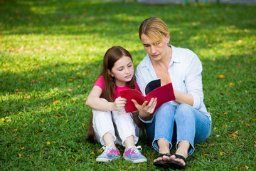 Fototapeta premium Mother and son are reading a book and smile at the park